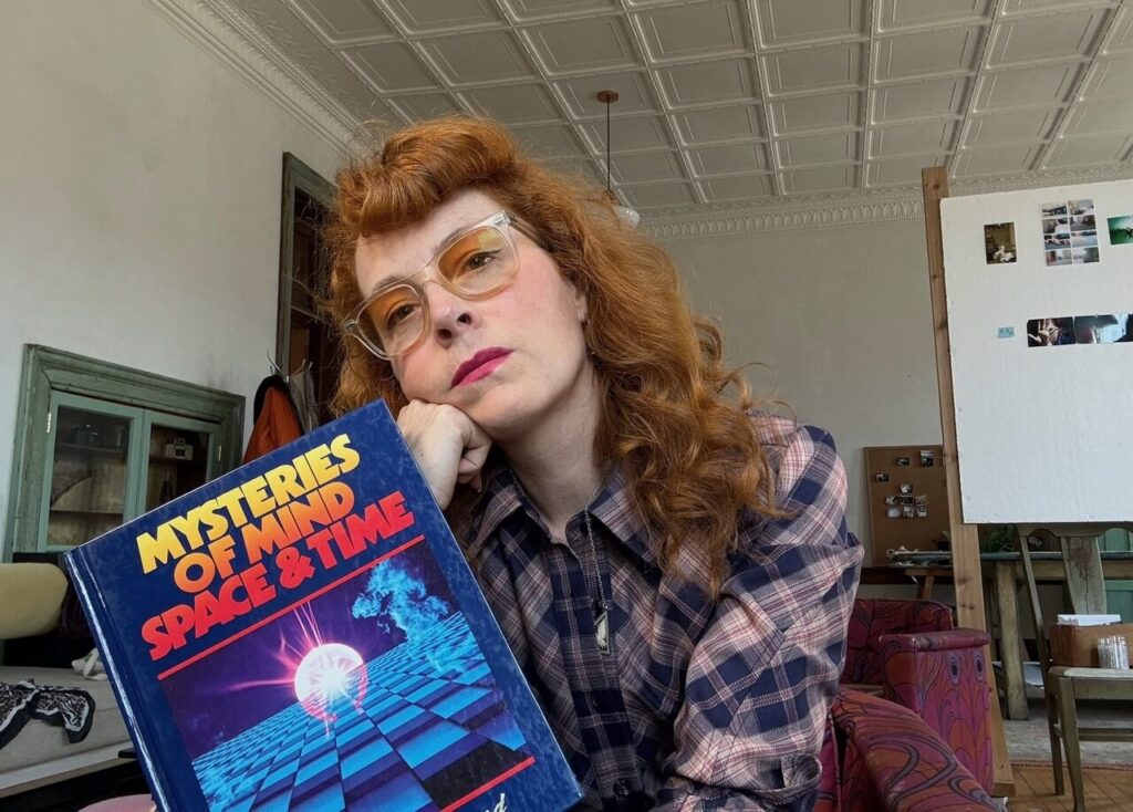 Melissa Auf Der Mar sits holding a book with her chin resting on her fist.